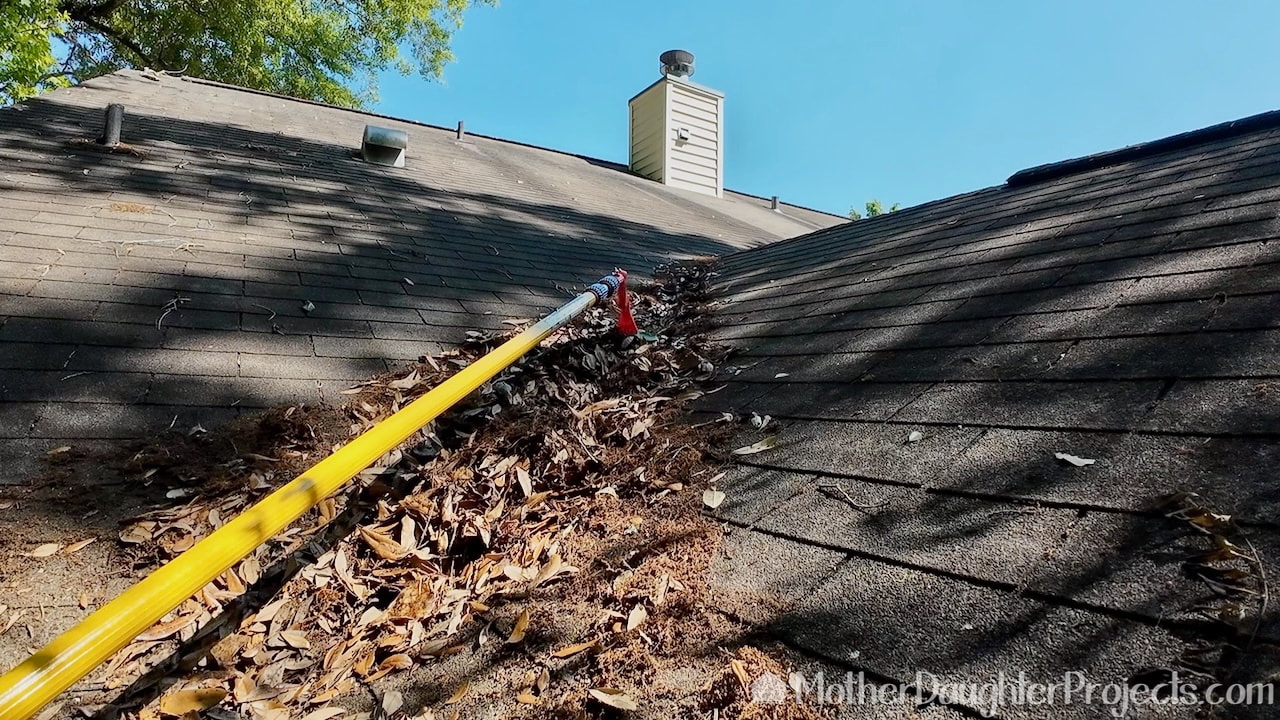 Manually removing the leaves and pollen from the roof valleys with a mini rake on an extension pole.