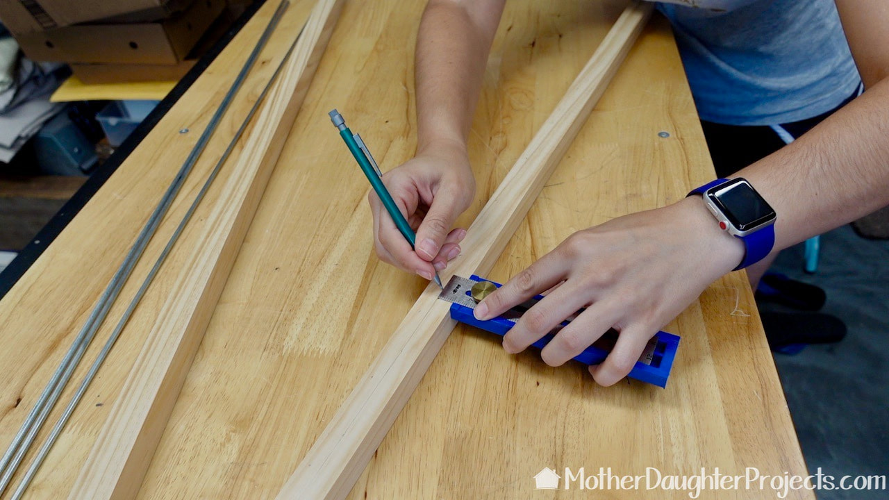 Steph is using a Kreg multi-mark to draw a line down the center of the wood dowel. 