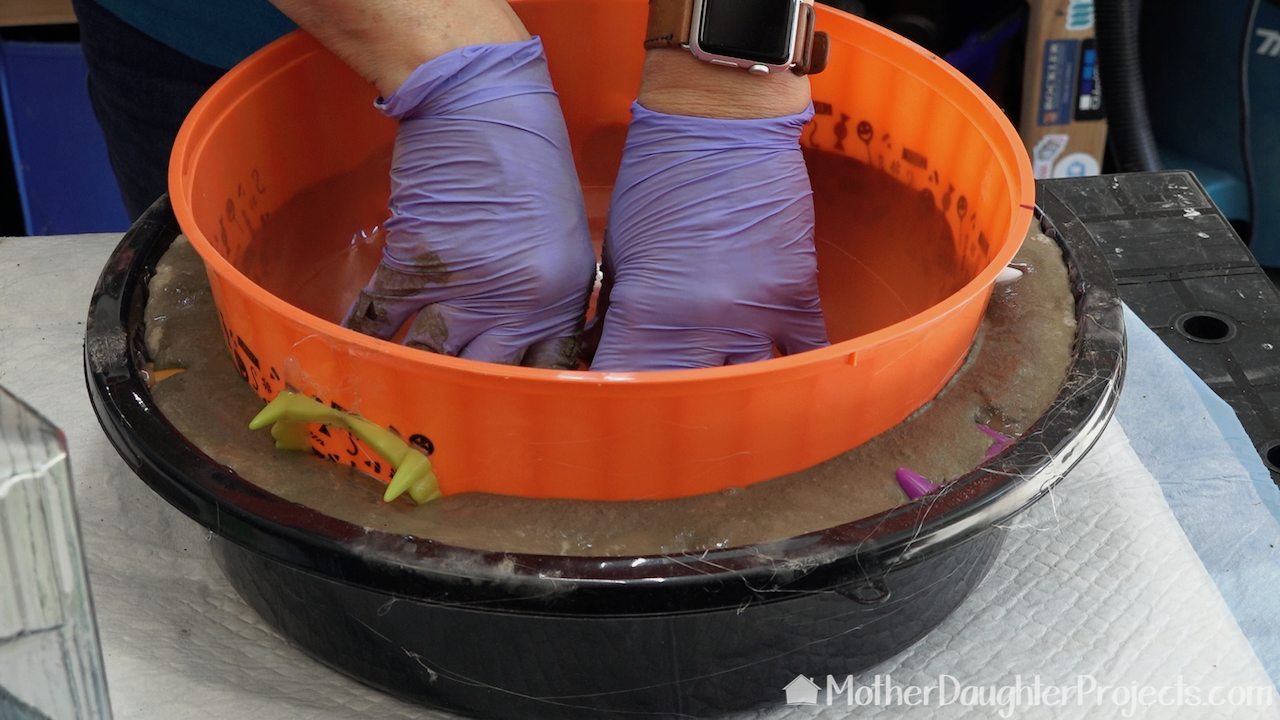 Fill the black container half full of concrete then push the orange bowl into place. Weight it down. 