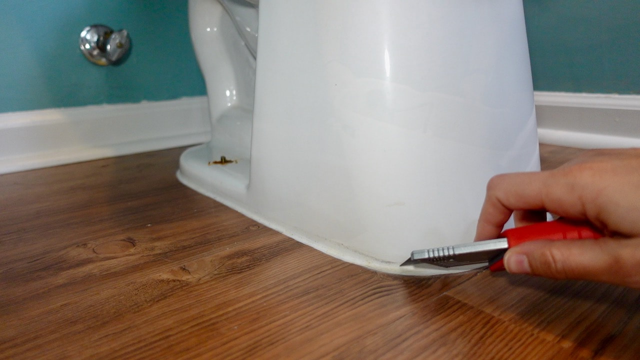 Cutting the caulk at the base of the toilet to break the seal.